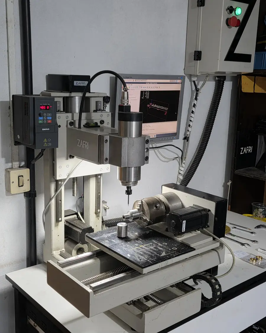 Fresa CNC de quatro eixos com o nome Zafri na estrutura e o programa aberto no monitor ao lado